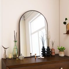 a mirror sitting on top of a dresser next to a vase and potted plant