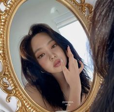 a woman with blue hair is looking at her reflection in a gold framed oval mirror