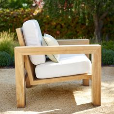 a wooden chair with white pillows on top of it in front of some bushes and trees