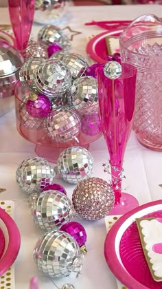 the table is set with pink and silver plates, wine glasses, and disco balls