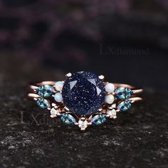 a ring with blue and white stones on it sitting on a black stone surface in front of a dark background