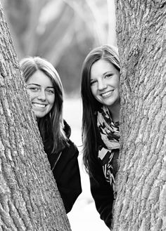 two women standing between two large trees in black and white, smiling at the camera