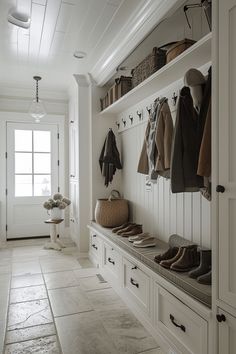 a hallway with white cabinets and coat racks filled with coats, shoes and sweaters