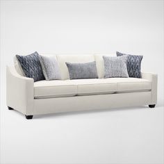 a white couch with several pillows on it's back and sides, in front of a gray background