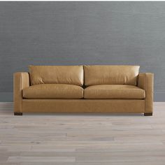 a tan leather couch sitting on top of a hard wood floor next to a gray wall