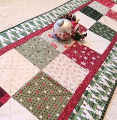 a christmas ornament sitting on top of a quilted table runner next to a pine cone