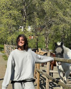 a woman standing next to a fence with two horses