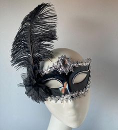 Classic masquerade mask, featuring a black plastic base with silver trim, faux black flower, large acrylic gem and single feather detail. Unisex mask with ribbon straps to tie in place. Made from a thick black plastic base mask, can be use over and over if stored carefully. Feather Masks, Black Masquerade Mask, Acrylic Gems, Costume Mask, Masquerade Mask, Black Flower, Black Feathers, Black Plastic, Costume Accessories