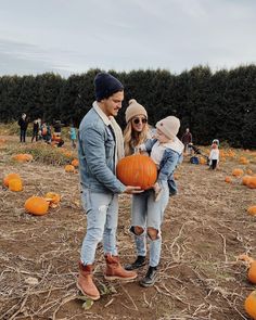 a man and woman holding a child in front of pumpkins on the ground with other people around them