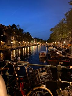 several bicycles are parked on the side of a canal at night with boats in the water