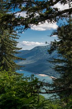 the view through some trees looking down on a lake and mountains in the distance with clouds