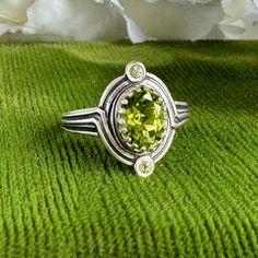 Vintage Art Deco details around every corner of this stunning ring! Hand forged in an antique impression die originally used in the early 1900's and reimagined with a high grade 1.5 carat Peridot natural gemstone center stone and 2 brilliant Peridot side stones. A sentimental beauty that you'll want to wear every day.  *Artisan all the way! *Hand forged in an antique impression die from the early 1900's *1.5 carat AA natural Peridot gemstone with (2) 2mm natural Peridot side stones *Solid recycl Antique Oval Three Stone Rings, Heirloom Green Three Stone Ring, Antique Three Stone Oval Jewelry, Antique Oval Three-stone Jewelry, Antique Three-stone Oval Jewelry, Elegant Three Stone Collectible Ring, Classic Hand Forged Oval Rings, Vintage Hand Forged Jewelry For Anniversary, Vintage Oval Three-stone Ring