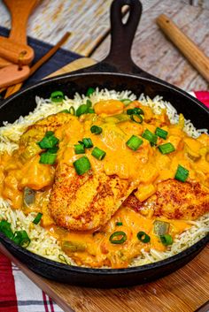 a skillet filled with chicken and rice on top of a wooden cutting board