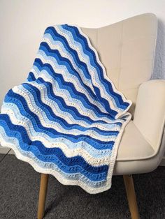 a blue and white crocheted blanket sitting on top of a chair next to a wall