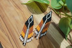 a pair of beaded earrings sitting on top of a wooden table next to a plant