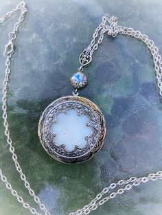 This beautiful locket is made with Baroque and Rococo eras in mind. The silver plated copper has been antiqued to bring out intricate details. The center carefully made to look like a blue iridescent moonstone or opal. It is framed by a scalloped lace edge Victorian style medallion. The light dances over it and the blue lavender flash is amazing. A filigree bail attaches the locket and the lavender AB crystal rhinestone to a nice long 34 inch chain. This can be doubled up to wear shorter if desi Vintage Metal Jewelry With Intricate Design, Silver Keepsake Amulet Jewelry, Metal Filigree Jewelry For Vintage Style, Metal Filigree Jewelry For Vintage Collection, Ornate Antique Silver Necklace With Antique Finish, Adjustable Antique Silver Jewelry With Antique Finish, Ornate Antique Silver Necklace, Elegant Antique Finish Round Locket Necklace, Elegant Antique Finish Round Pendant Locket Necklace