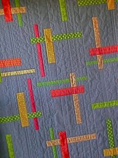 a quilted wall hanging on the side of a bed with colorful strips in it