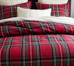 a bed with red and green plaid comforter on top of it, next to a night stand