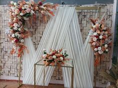 an arrangement of flowers on display in front of a wall with white drapes and curtains