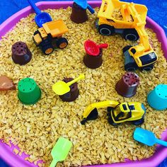 a pink tray filled with lots of toys on top of a blue table covered in rice