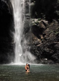 two people standing in front of a waterfall