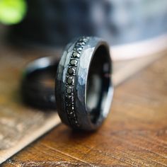 a wedding band with black diamonds on it sitting on a wooden table next to a knife