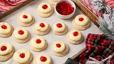 cookies with white frosting and cherry toppings on a baking sheet next to christmas decorations