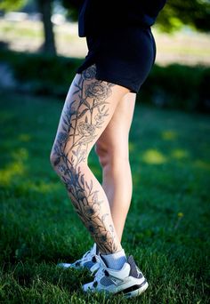 a woman with tattoos on her legs and leggings is standing in the grass