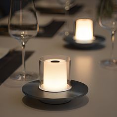 a lit candle sits on a plate at a table with wine glasses and water in the background