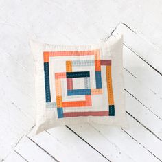 a white pillow with an orange and blue patchwork design on the front sitting on a wooden floor