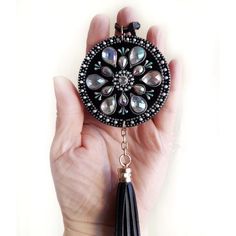 a hand holding a black and white brooch with tassels