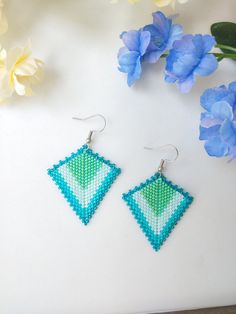 a pair of blue and green earrings sitting on top of a table next to flowers