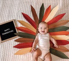 a baby laying on top of a bed next to a sign that says happy thanksgiving