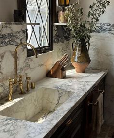 a bathroom with marble counter tops and gold faucets on the sink, along with a vase filled with flowers