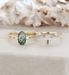 two gold rings with green and white stones on top of each other next to dried flowers