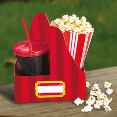 a red box with popcorn and a drink in it sitting on a wooden table outside