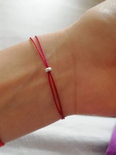 a woman's arm wearing a red string bracelet with a white bead on it