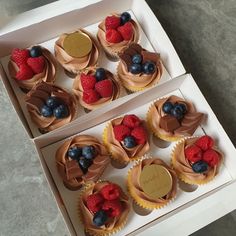 cupcakes with chocolate frosting and fresh berries are displayed in a box on the table