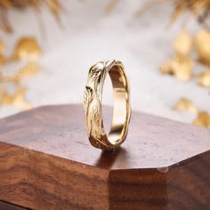 a gold wedding ring sitting on top of a wooden box with golden leaves around it