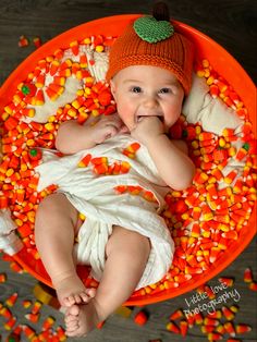 a baby laying in an orange bowl with candy corn all over it's body