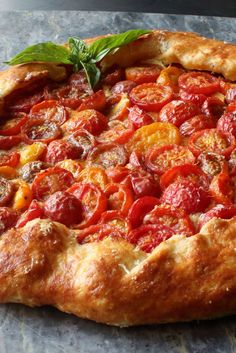 a pizza with tomatoes and basil on it sitting on top of a stone countertop