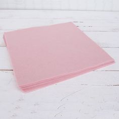 a stack of pink napkins sitting on top of a white wooden table next to a bottle