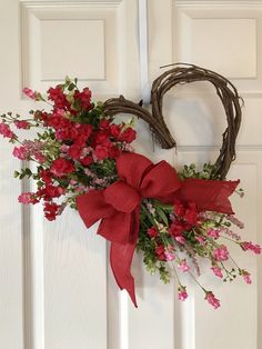 a heart shaped wreath with red flowers hanging on the front door