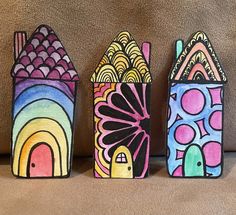 three small houses painted in different colors on a brown surface, one has a bird and the other is a fish