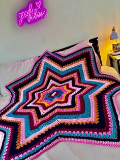 a crocheted blanket sitting on top of a bed next to a neon sign