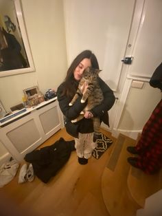 a woman holding a cat in her arms while standing on a wooden floor next to a door