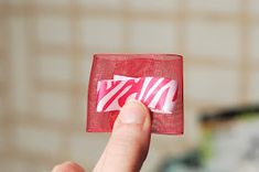 a hand is holding up a small piece of red material with zebra print on it