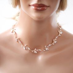 a mannequin wearing a necklace with leaves and pearls on the neck, in front of a white background