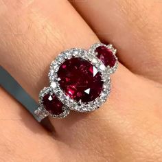 a woman's engagement ring with two oval cut red stones on the center and sides