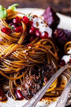 a plate full of spaghetti with meat and vegetables on it, next to silverware